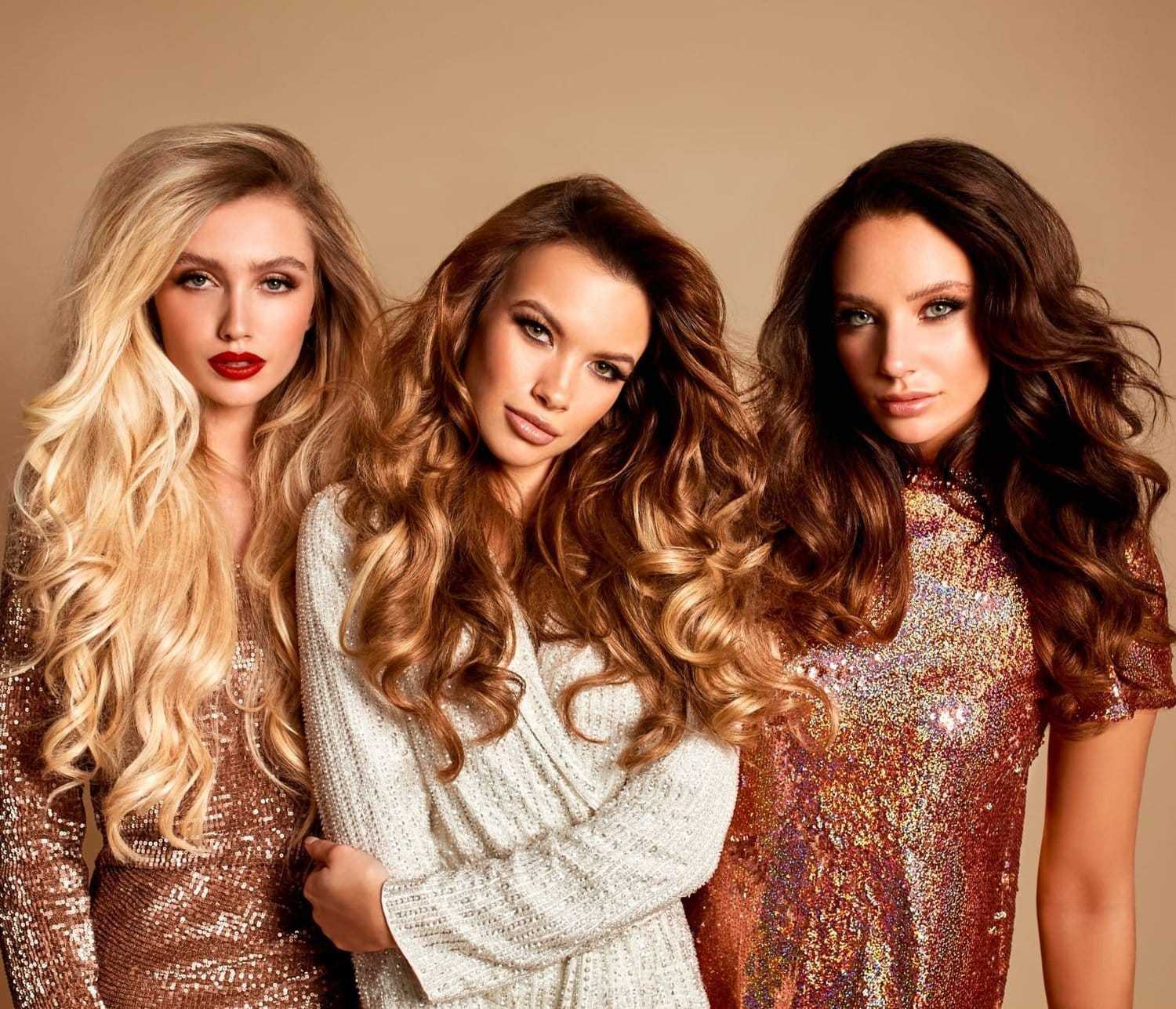 Three women with styled hair and elegant outfits posing against a plain background.