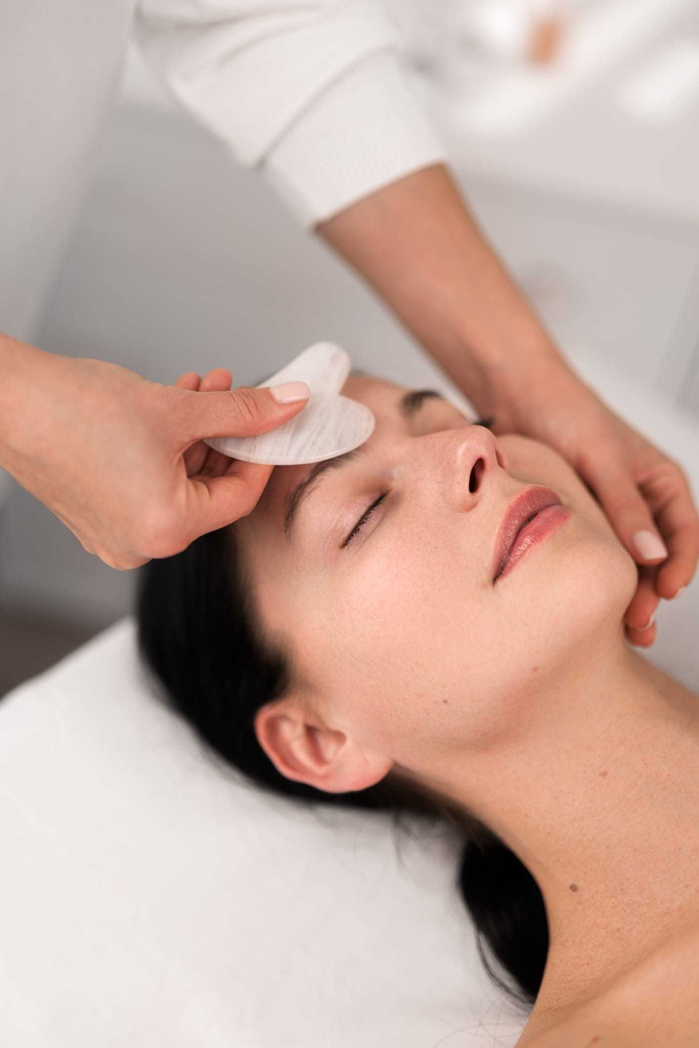 Facial massage using a white stone tool on a relaxed woman.